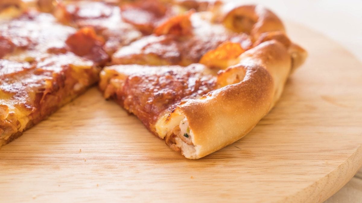 Cheese Crust Pizza Pan Pizza Pizza Hut mit Peperoniwurst und Käserand angeschnitten auf Holzbrett. Draufsicht.