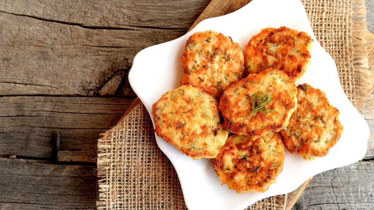 Draufsicht: Gebratene dänische Fischbuletten, also Fiskefrikadeller, auf einem weißen Teller auf groben Leinentuch, das auf einem Holzboden liegt.