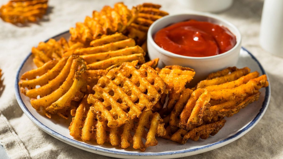 Ein Teller Gitterkartoffeln mit einem Schälchen Ketchup.