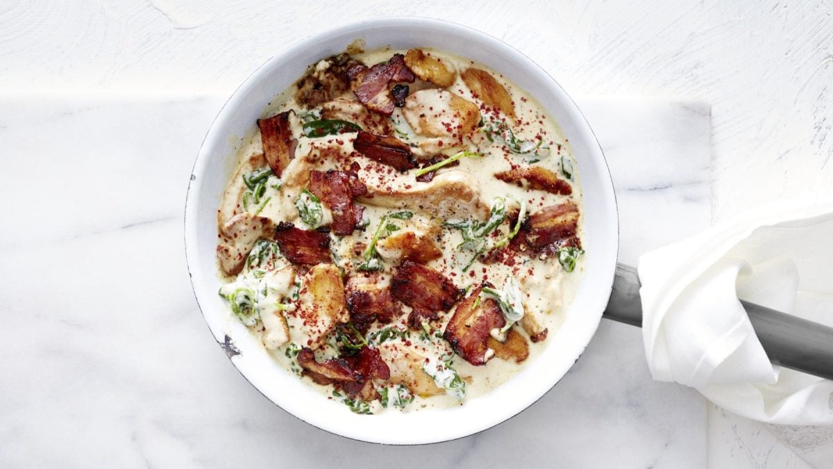 Keto-Hähnchen in Spinat-Sahnesauce in einer weißen Pfanne vor einem weißen Hintergrund.