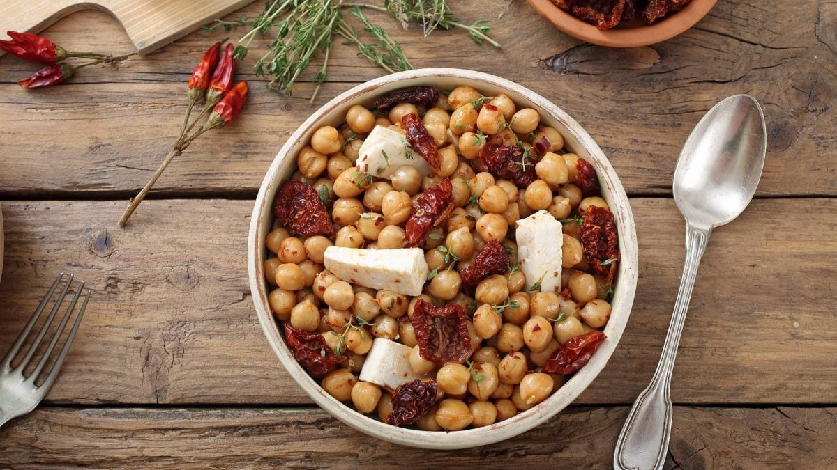 Eine weiße Schale mit dem Salat direkt von oben fotografiert. Darüber Feta, getrocknete Tomaten und Thymian. Alles auf einem rustikalen Holztisch.