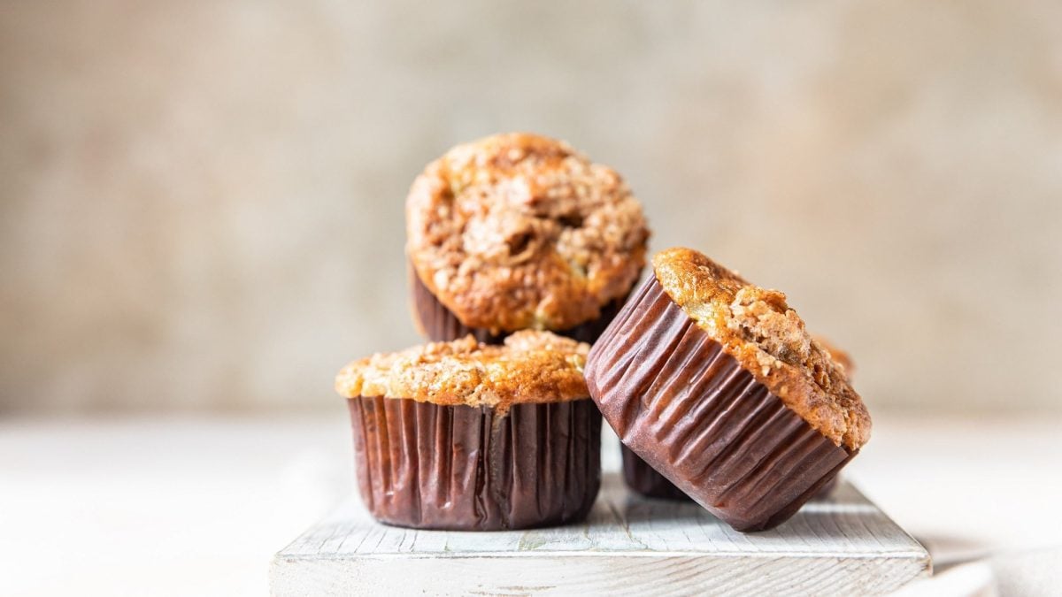 3 Kürbismuffins mit Streuseln auf einem weoßen Brett vor hellem Hintergrund.