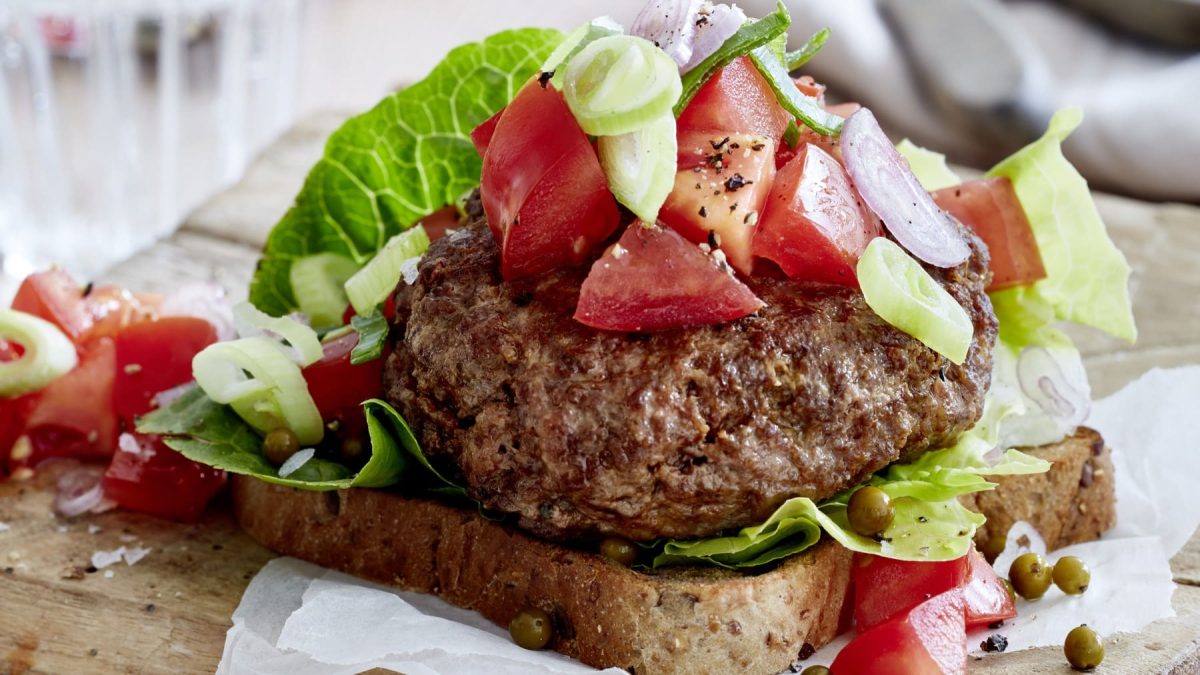 Ein leichter Beef-Burger mit grünem Pfeffer auf einem braunen Schneidebrett.