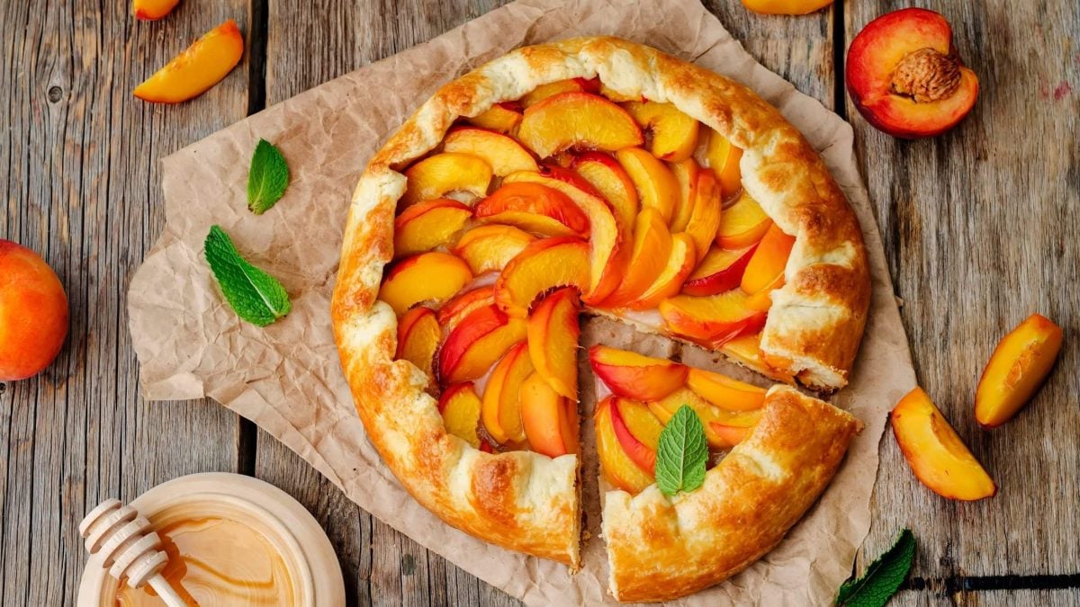 Draufsicht: eine Pfirsich-Galette auf Backpapier auf einem Holztisch.