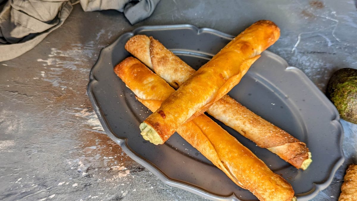 Knusprige Wrap-Rollen mit cremiger Guacamole auf einem grauen, ovalen Teller und Steinuntergrund.