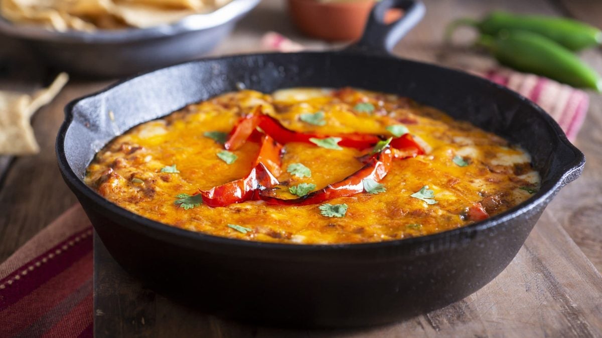 Queso fundido in schwarzer Gussform auf Holz. Im Bild Chilis und Brot. Draufsicht.