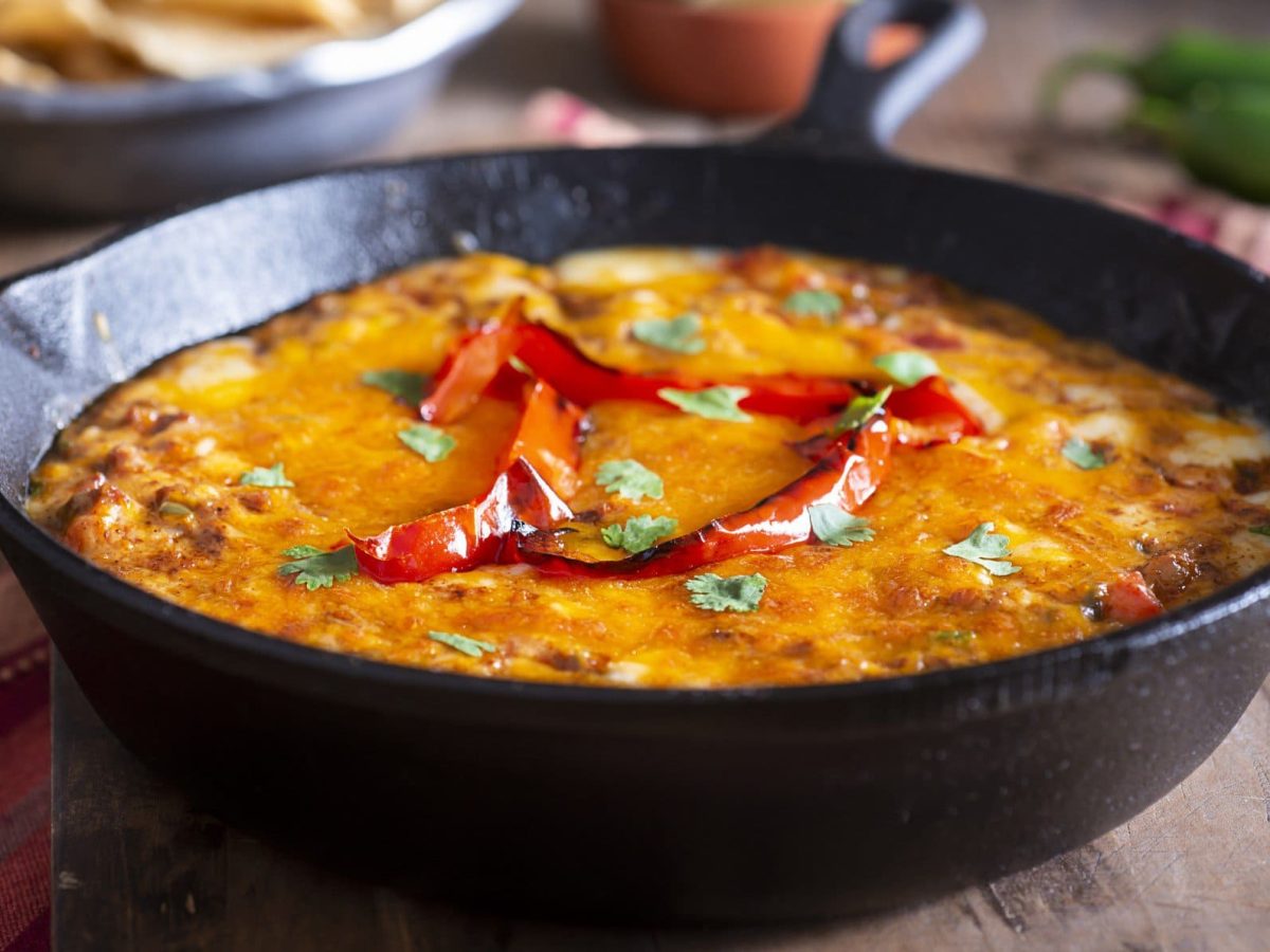 Queso fundido in schwarzer Gussform auf Holz. Im Bild Chilis und Brot. Draufsicht.