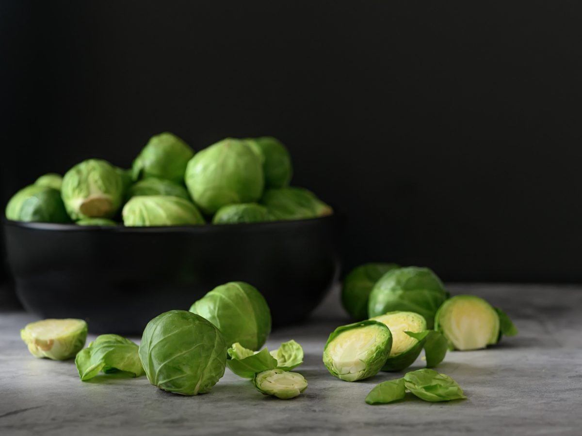 Rosenkohl in einer schwarzen Schüssel auf grauem Untergrund und vor schwarzem Hintergrund nah und von der Seite fotografiert.