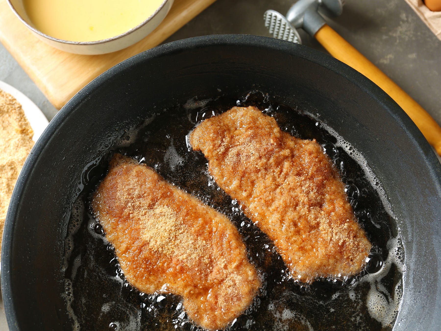 Zwei Schnitzel die in der Pfanne braten, direkt von oben fotografiert.