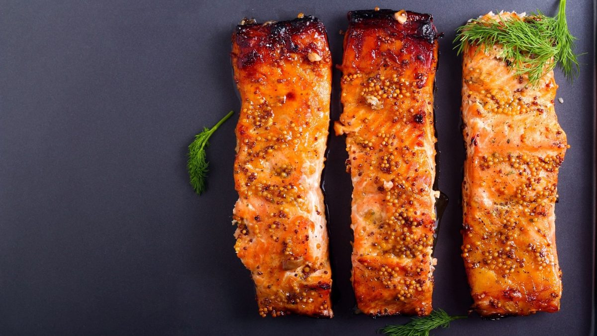 Drei Stück Honig-Senf-Lachs auf einem dunklen Untergrund.