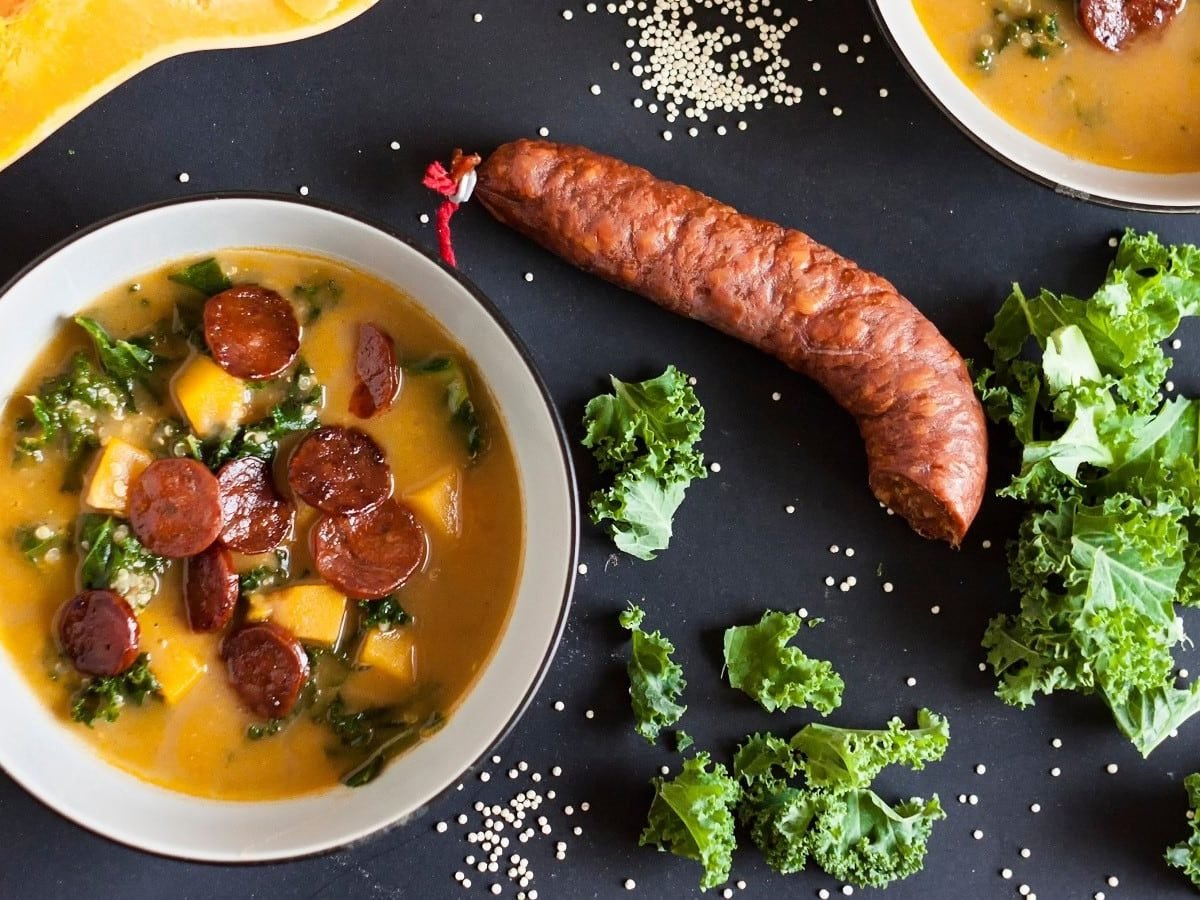 Eine weiße Suppenschüssel mit einer Portion Chorizo-Kürbissuppe auf einem dunklen Tisch.