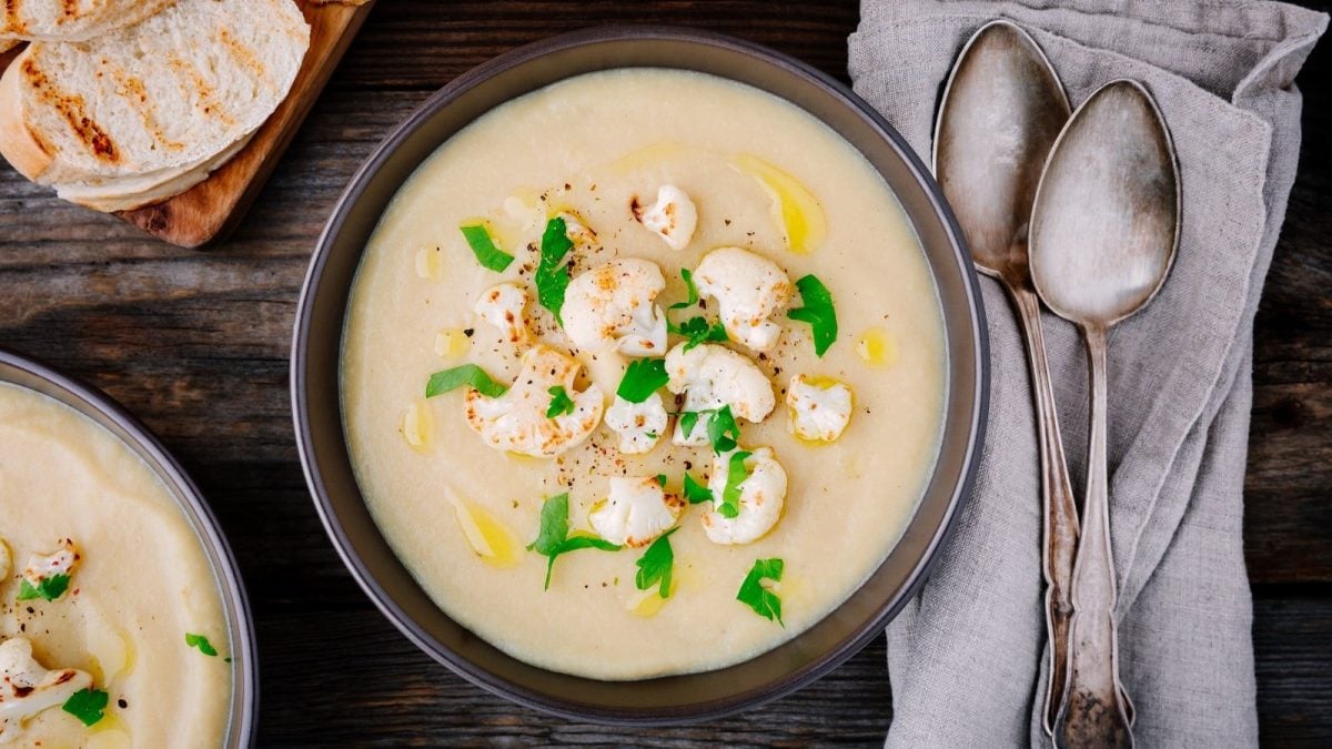 Ein tiefer Teller mit einer Portion Kokos-Blumenkohl-Suppe auf einem Holztisch.