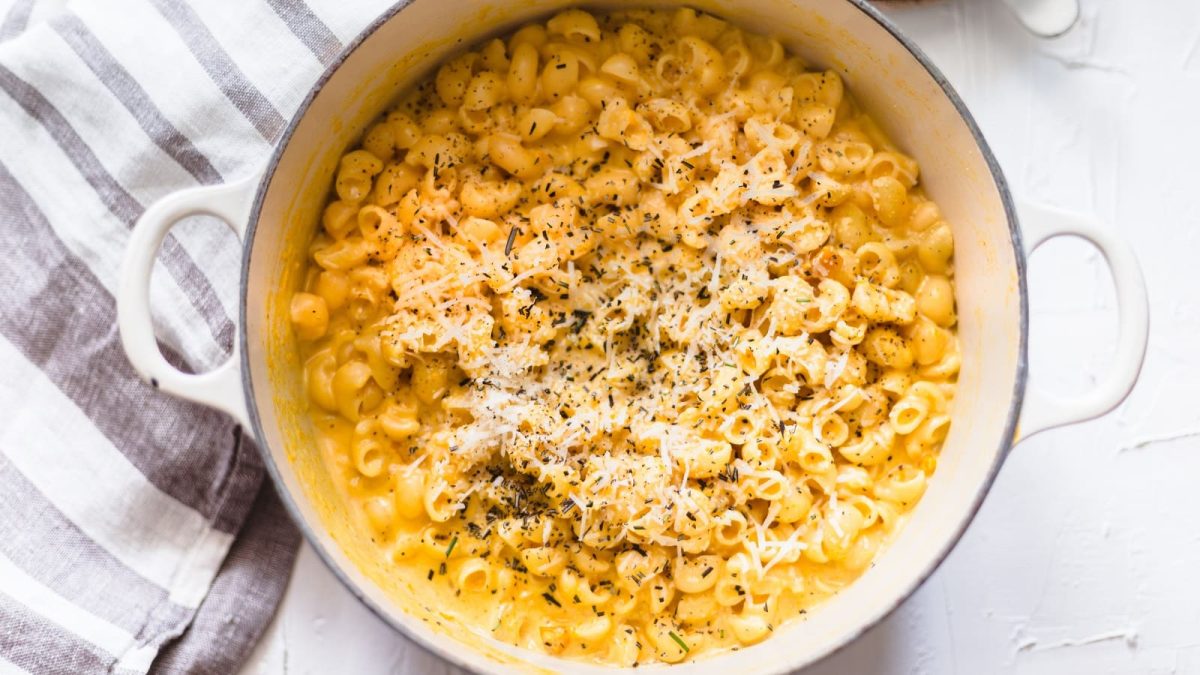 Ein weißer Topf mit Kürbis Mac and Cheese auf einem Küchentuch.