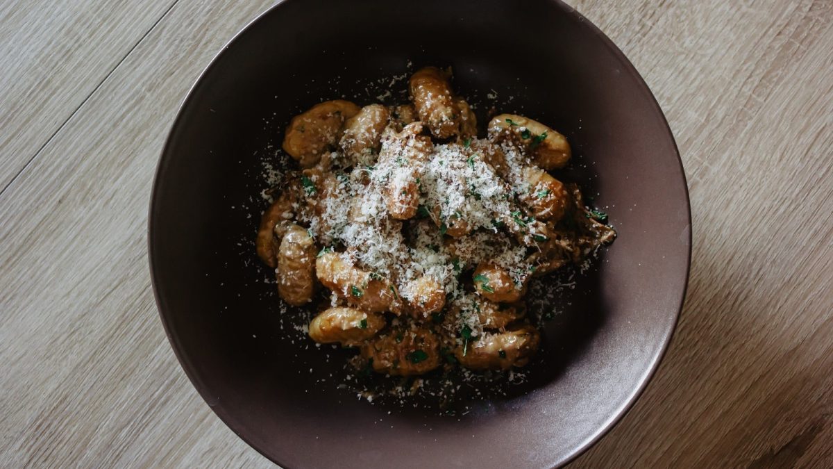 Ein brauner Teller mit Gnocchi in Nussbutter auf einem Holztisch.