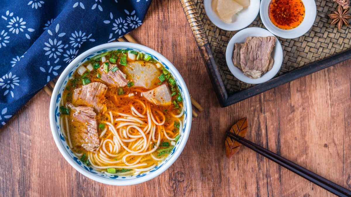 Eine Portion Lanzhou-Nudelsuppe n einer blauen Schüssel auf einem Holztisch.