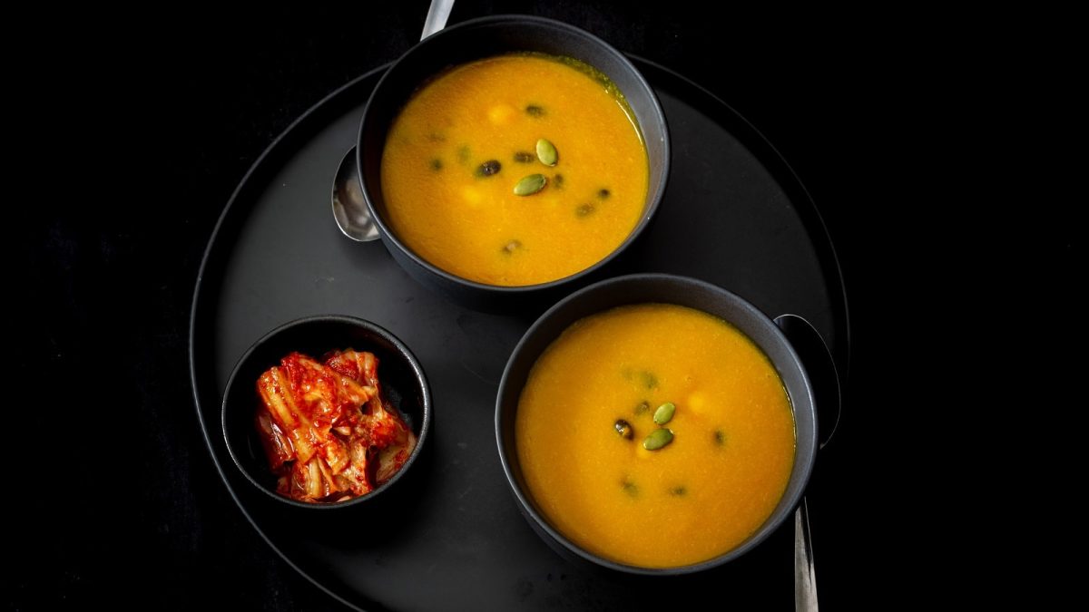 Zwei schwarze Schüsseln mit Hobakjuk neben einer Schale Kimchi.