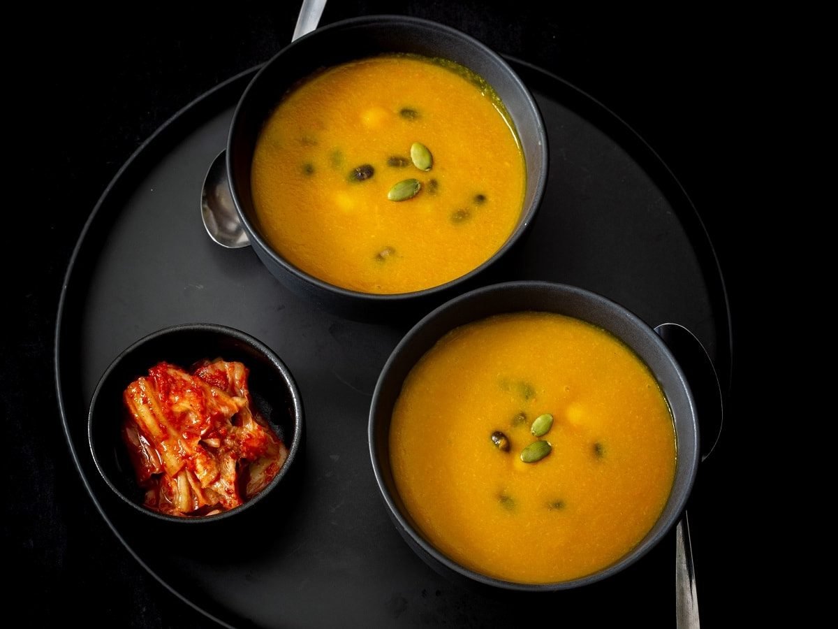 Zwei schwarze Schüsseln mit Hobakjuk neben einer Schale Kimchi.