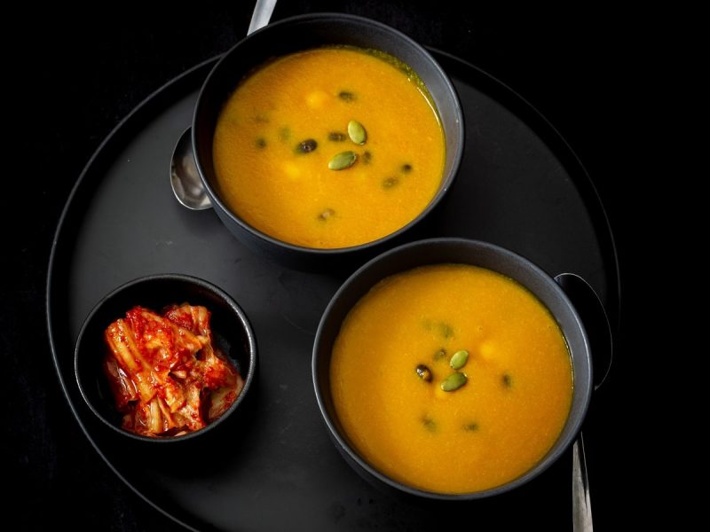 Zwei schwarze Schüsseln mit Hobakjuk neben einer Schale Kimchi.