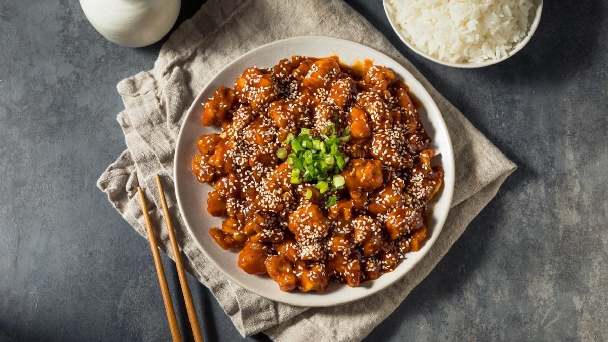 Ein weißer Teller mit Gochujang Chicken auf einem grauen Tisch.