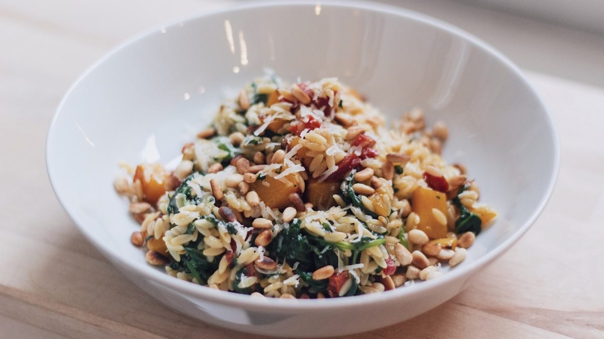Ein weißer tiefer Teller mit einer Portion Orzo-Pfanne mit Kürbis und Spinat.