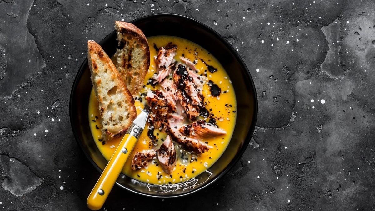 Eine schwarze Schüssel mit Lachs-Kürbissuppe auf einem grauen Untergrund.