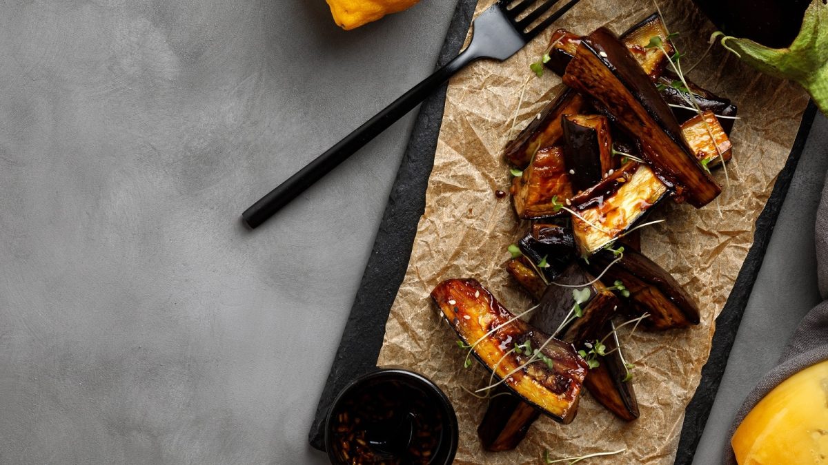 Ein schwarzes Schiefertablett mit Auberginen-Unagi auf einem grauen Tisch.