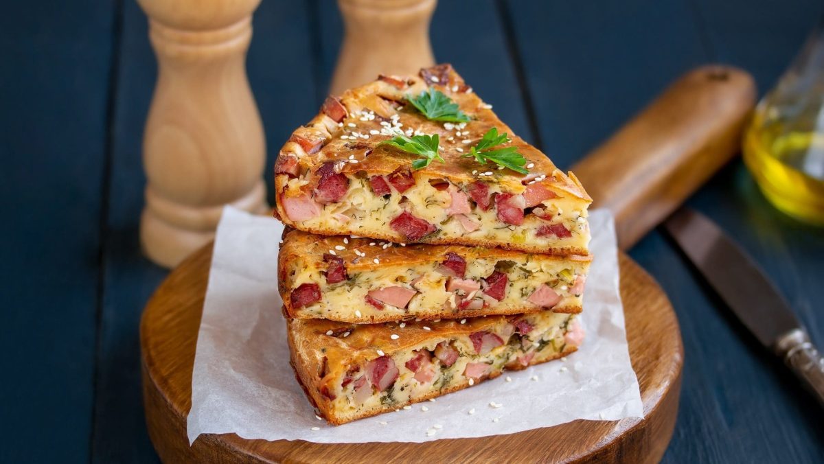 Frontal: Drei dreieckige Stücke britischer Bacon-Cheese Cake liegen aufeinandergestapelt auf einem Holzstuhl.