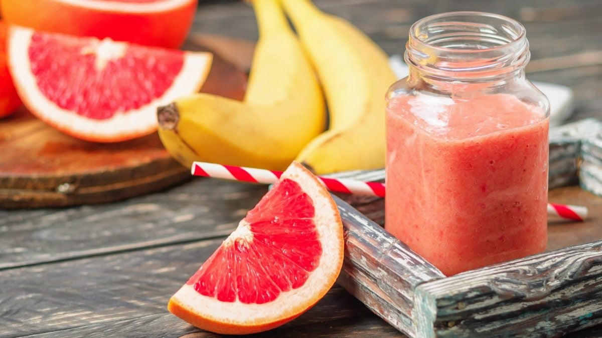 Frontal: Ein großes Glas mit einem Grapefruit-Bananen-Smoothie. Drumherum liegen Bananen und Grapefruits.