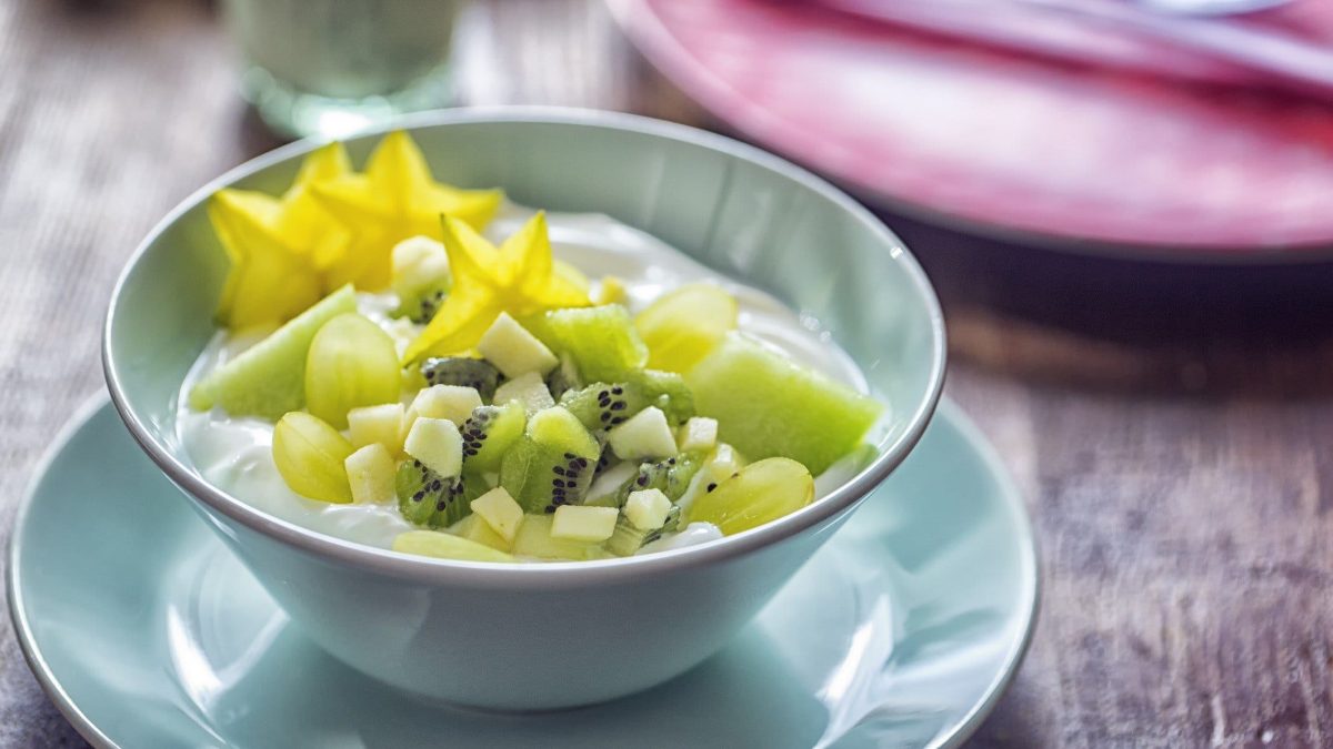 Draufsicht: ein Früchte-Frühstück mit Skyr in einer hellblauen Schüssel, die auf einem passenden Unterteller steht.