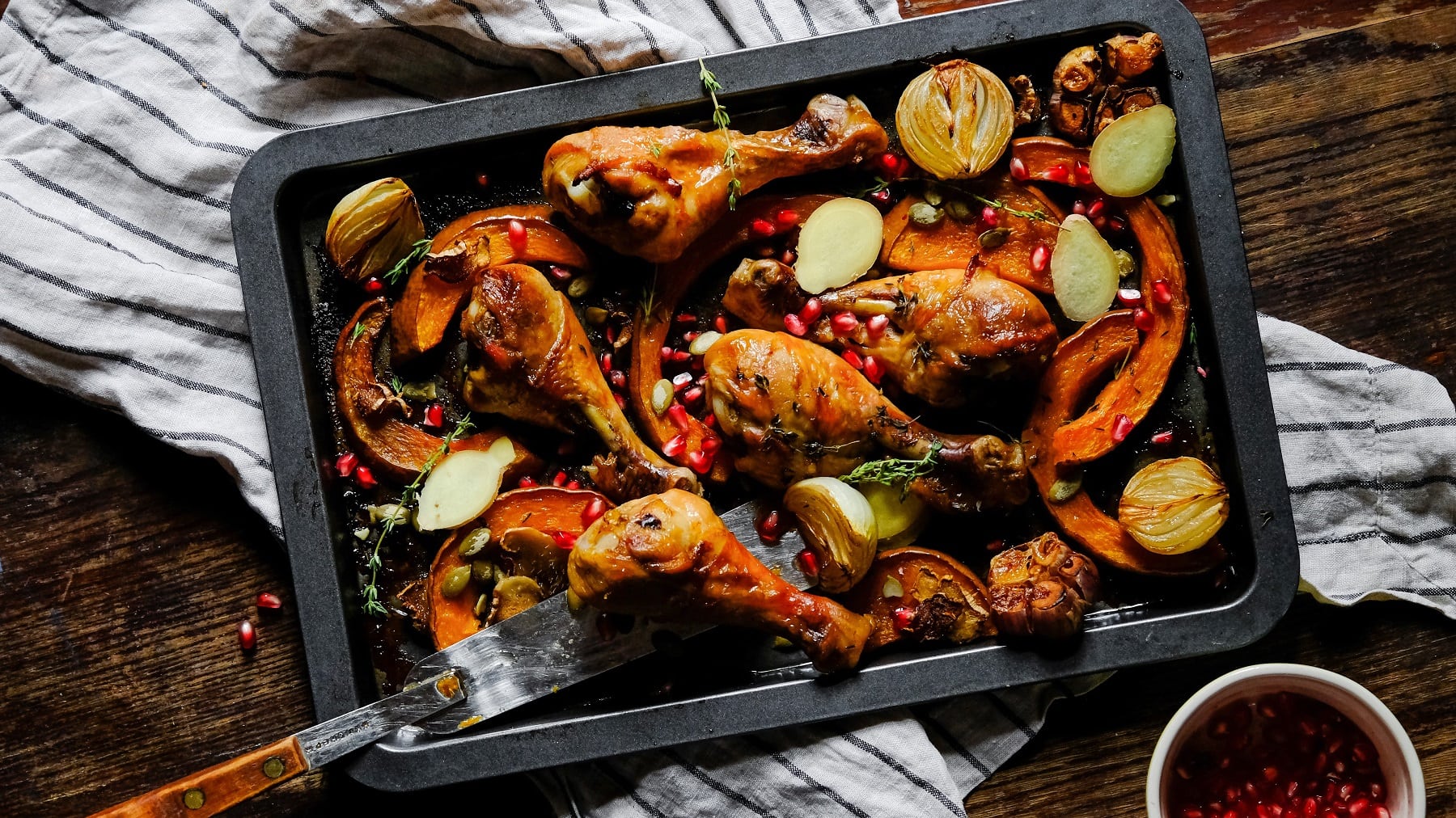 Ein Blech mit dem Kürbis und Hähnchen direkt von oben auf einem rustikalen Holztisch fotografiert.