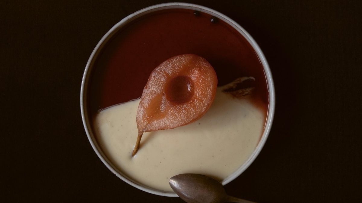 Eine Schüssel mit einer Gewürzbirne in Rotweinsud mit Vanillesauce, dunkler Untergrund, Draufsicht.