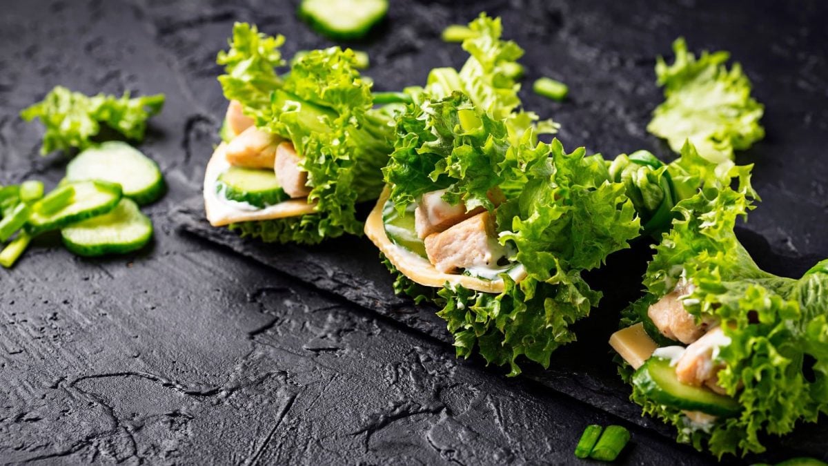 3 griechische Salat-Wraps mit Gyros, Gurkenscheiben und weiteren Zutaten gefüllt auf einem Brett.