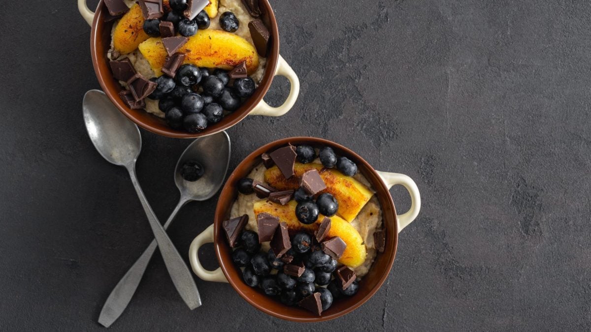 Zwei Schüsseln mit Grießbrei mit karamellisierter Banane auf dunklem Hintergrund. Links davon zwei Esslöffel.