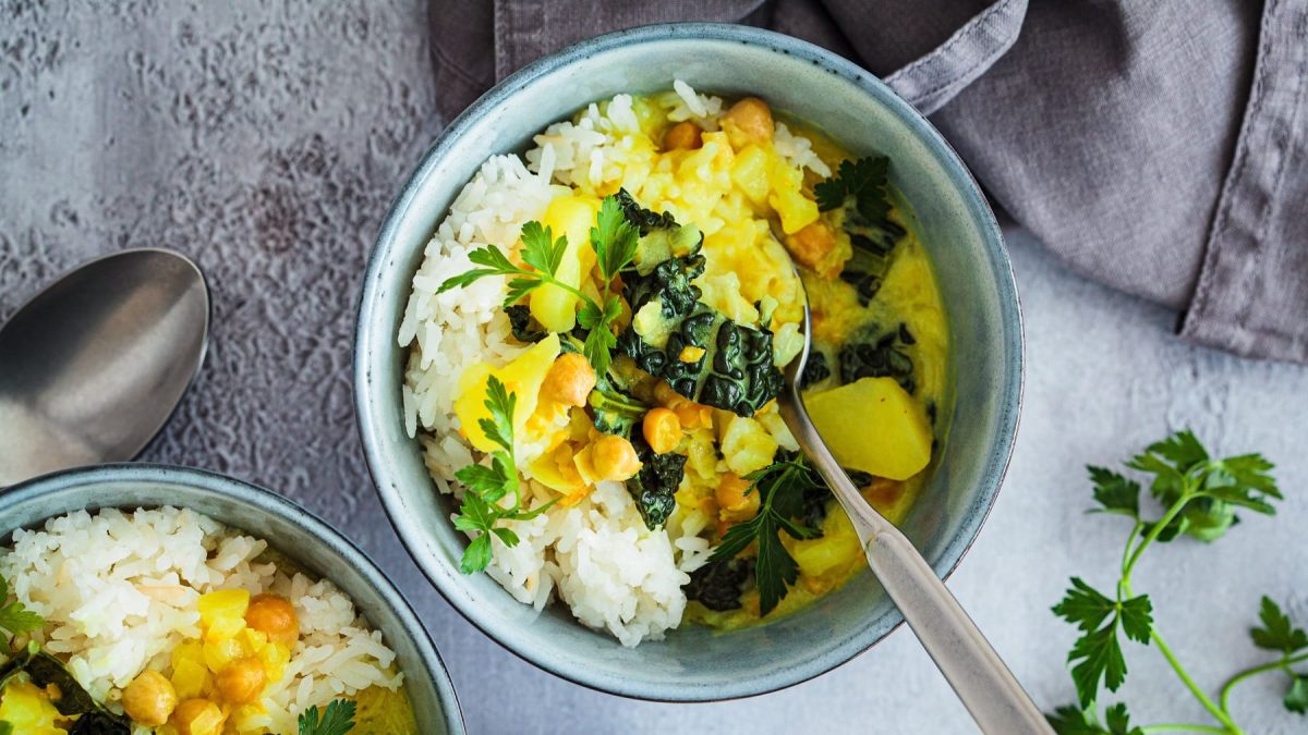 Eine hellblaue Schale mit dem Kartoffel-Curry auf grauem Untergrund direkt von oben fotografiert.