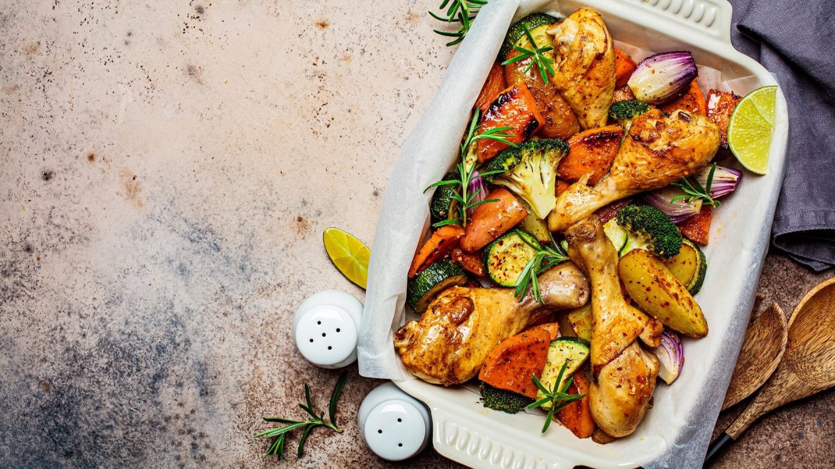 Eine weiße Auflaufform mit dem Limetten-Hähnchen und geröstetem Gemüse auf einem grau-beigen Tuch. Alles direkt von oben fotografiert.
