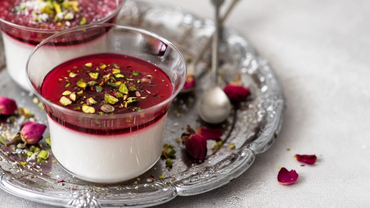 Draufsicht, schräg: Zwei Dessertgläser mit Malabi ,stehen auf einem orientalisch angehauchtem Tablett aus Metall. Drum herum liegen Rosenblüten.