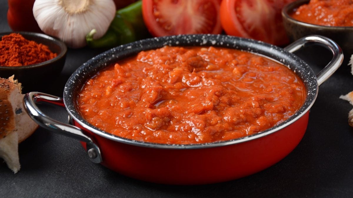 Ein kleines Pfännhcne mit der Tomatensalsa auf dunklem Untergrund mit rotem Gemüse im Hintergrund.