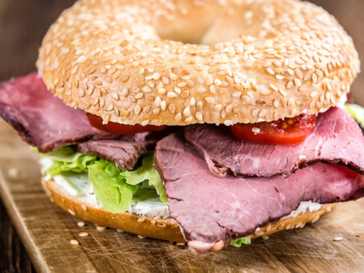 Draufsicht schräg: Ein Pastrami-Bagel auf einem Holzbrettchen.