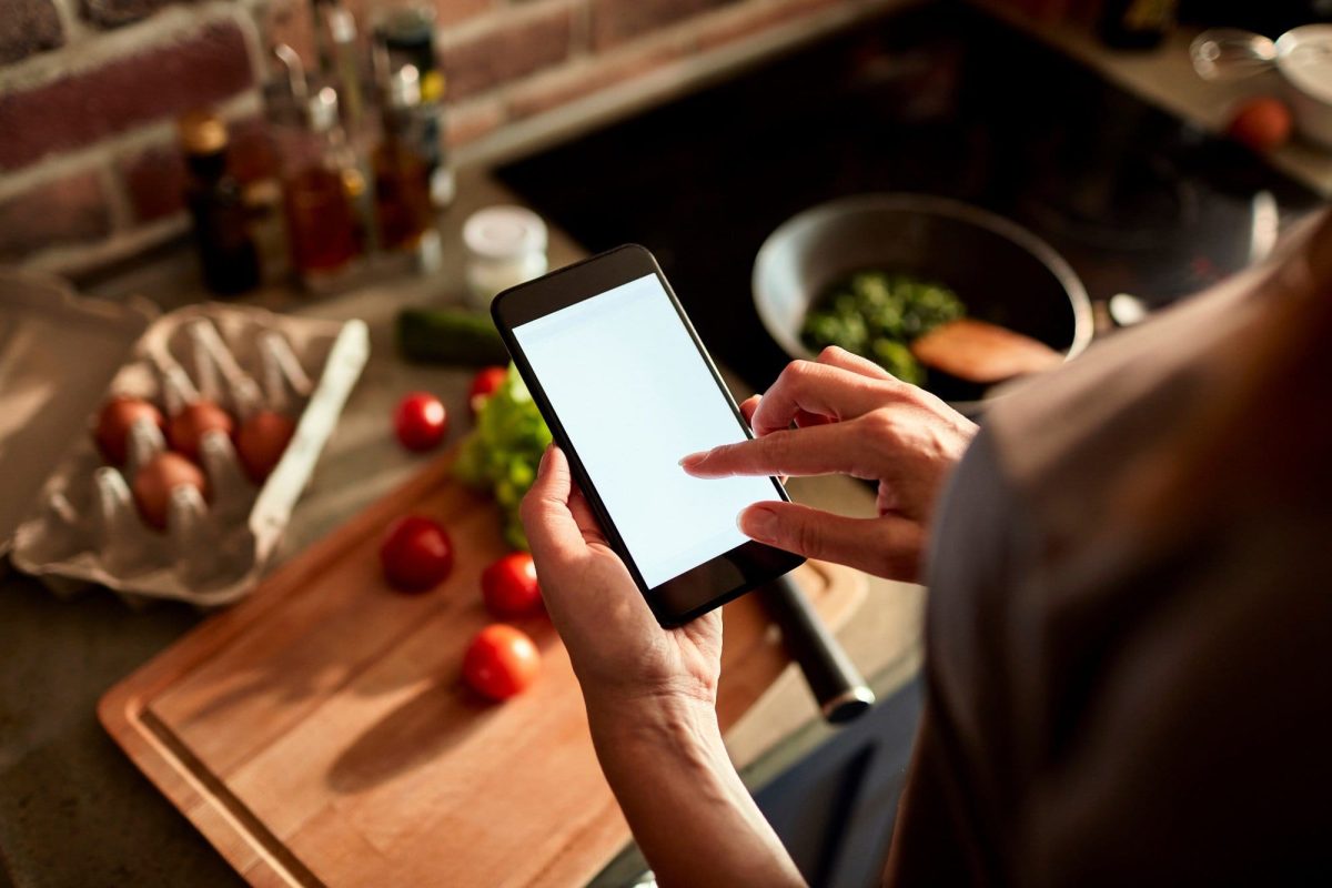 Frau schaut auf ihr Handy beim Kochen.