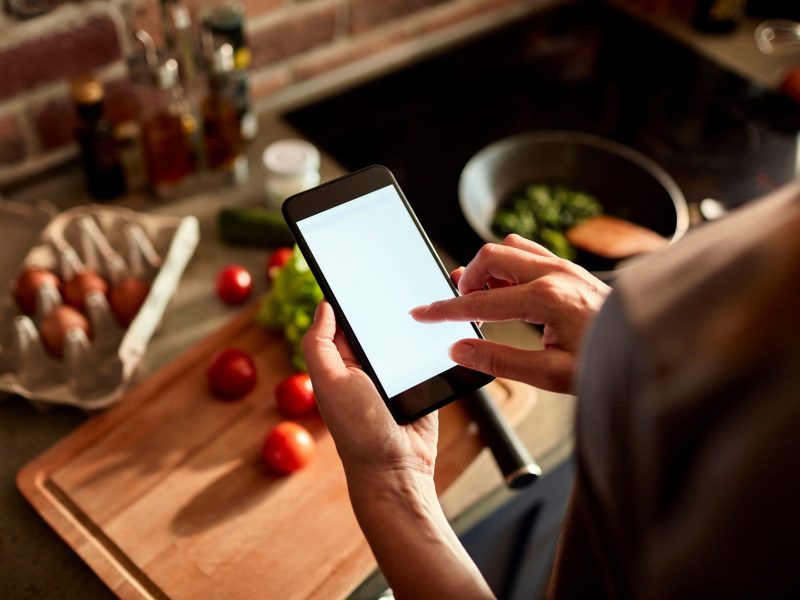 Frau schaut auf ihr Handy beim Kochen.