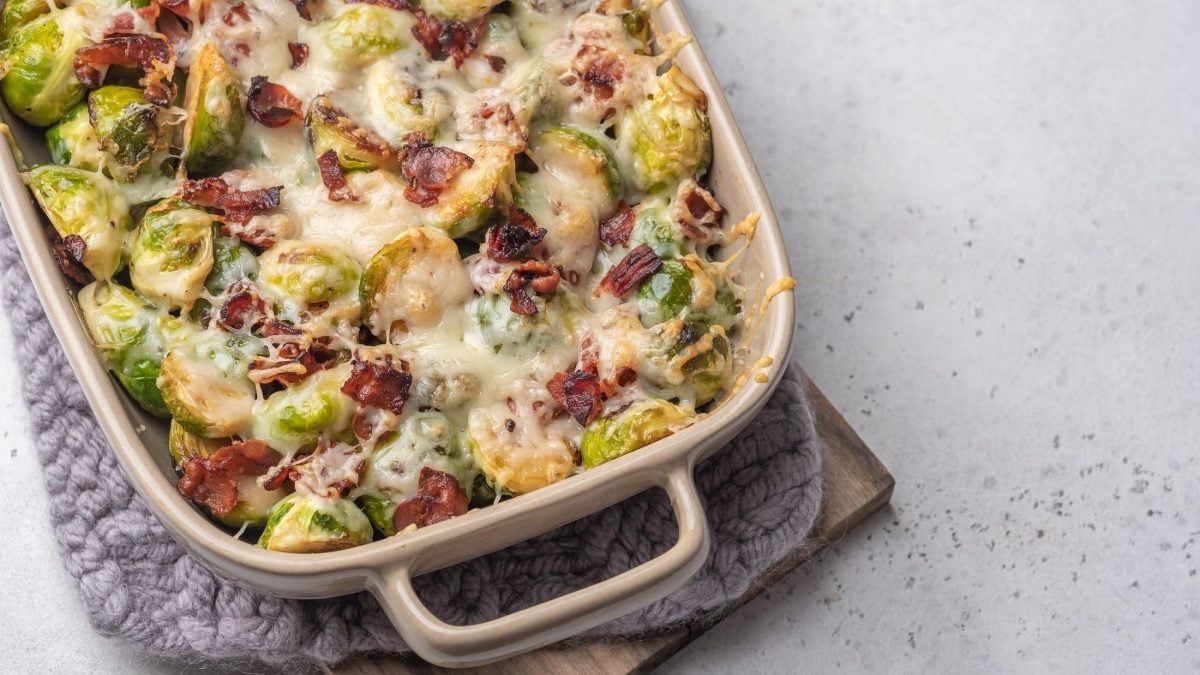 Draufsicht: Heller Untergrund und die Hälfte eines Rosenkohl-Gratin mit Kasseler in der Form.