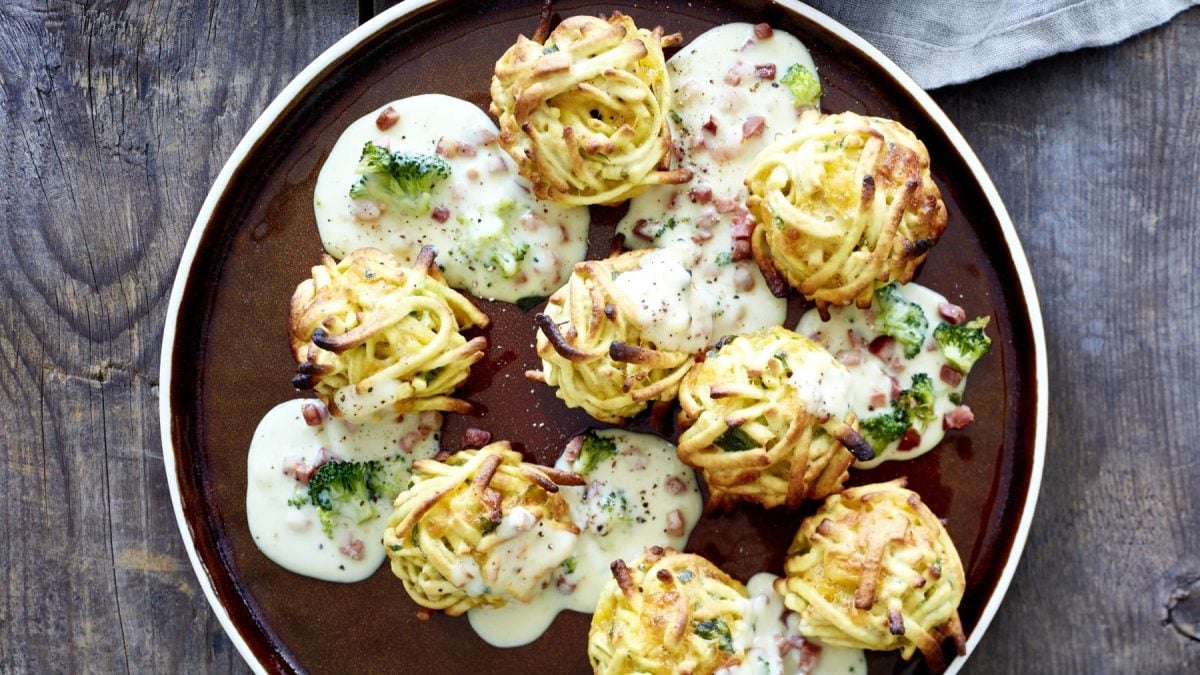 Spätzle-Cheddar-Balls mit Brokkoli-Schinken-Sauce auf dunklem Teller, darunter Holz.
