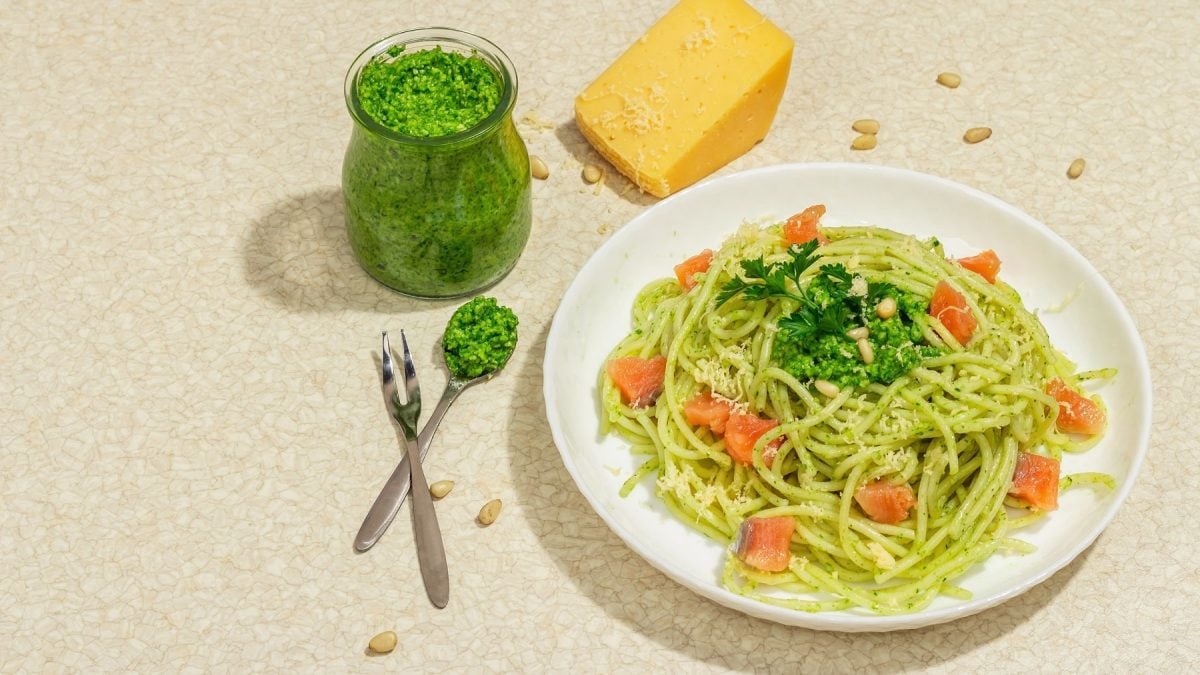 Ein weißer Teller mit den Spaghetti sowie Lachswürfeln und Lauch-Pesto auf beigem Untergrund.