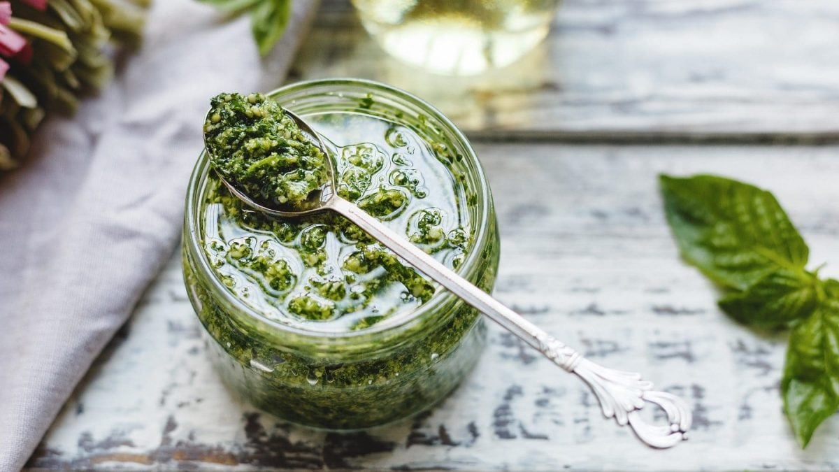 In einem Glas ist eine Spinat-Pesto. Auf dem Glas liegt ein Löffel. Neben dem Glas liegt ein Blass Spinat.