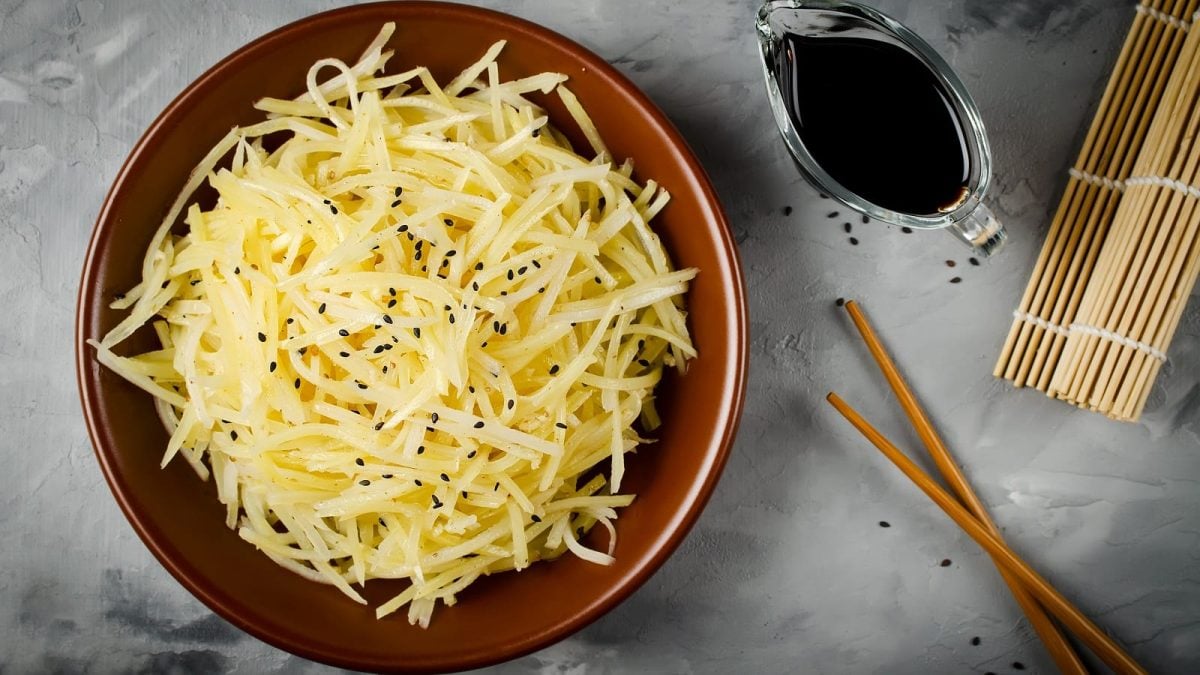 Ein brauner Teller mit chinesischem Kartoffelsalat auf einem grauen Untergrund.
