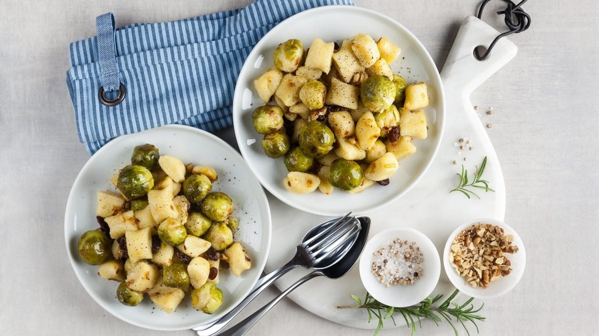 Zwei Teller Gnocchi-Rosenkohl-Pfanne neben einem blauen Küchentuch.