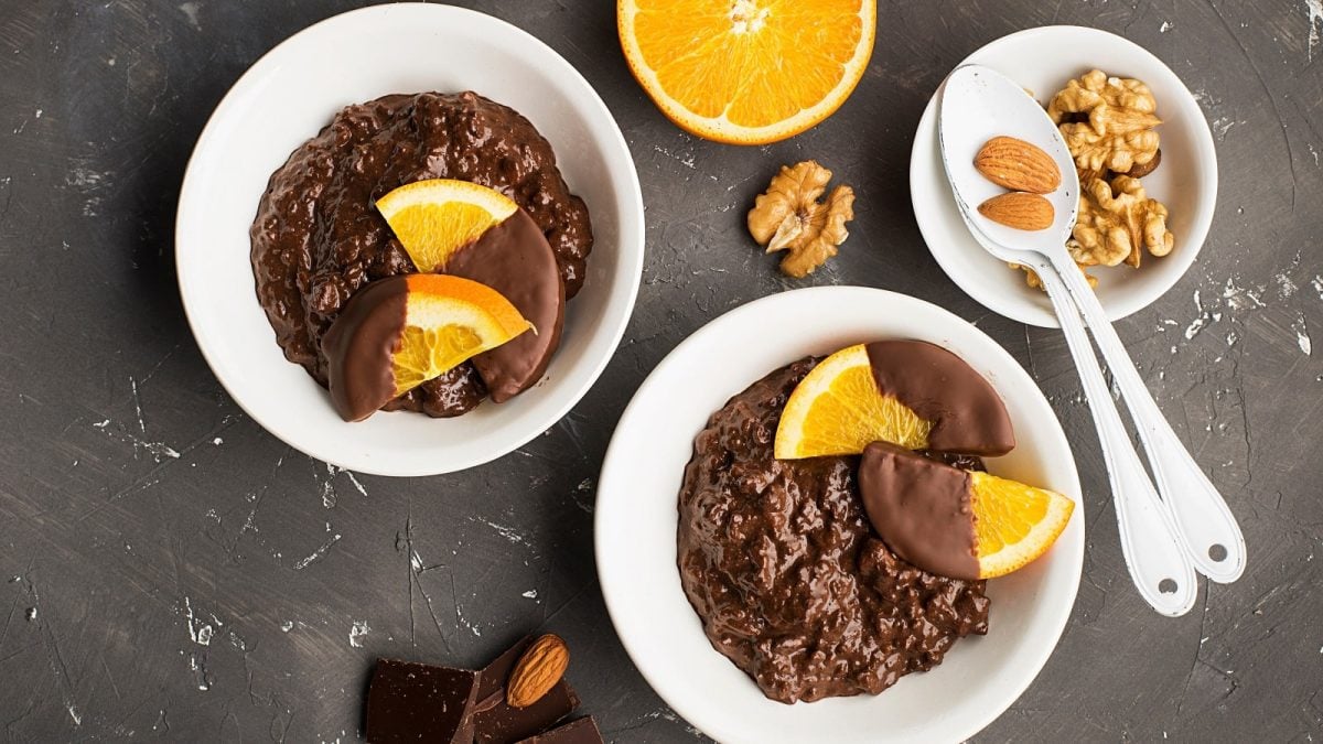 Zwei Schüsseln mit Orangen-Schoko-Porridge auf einem grauen Tisch.