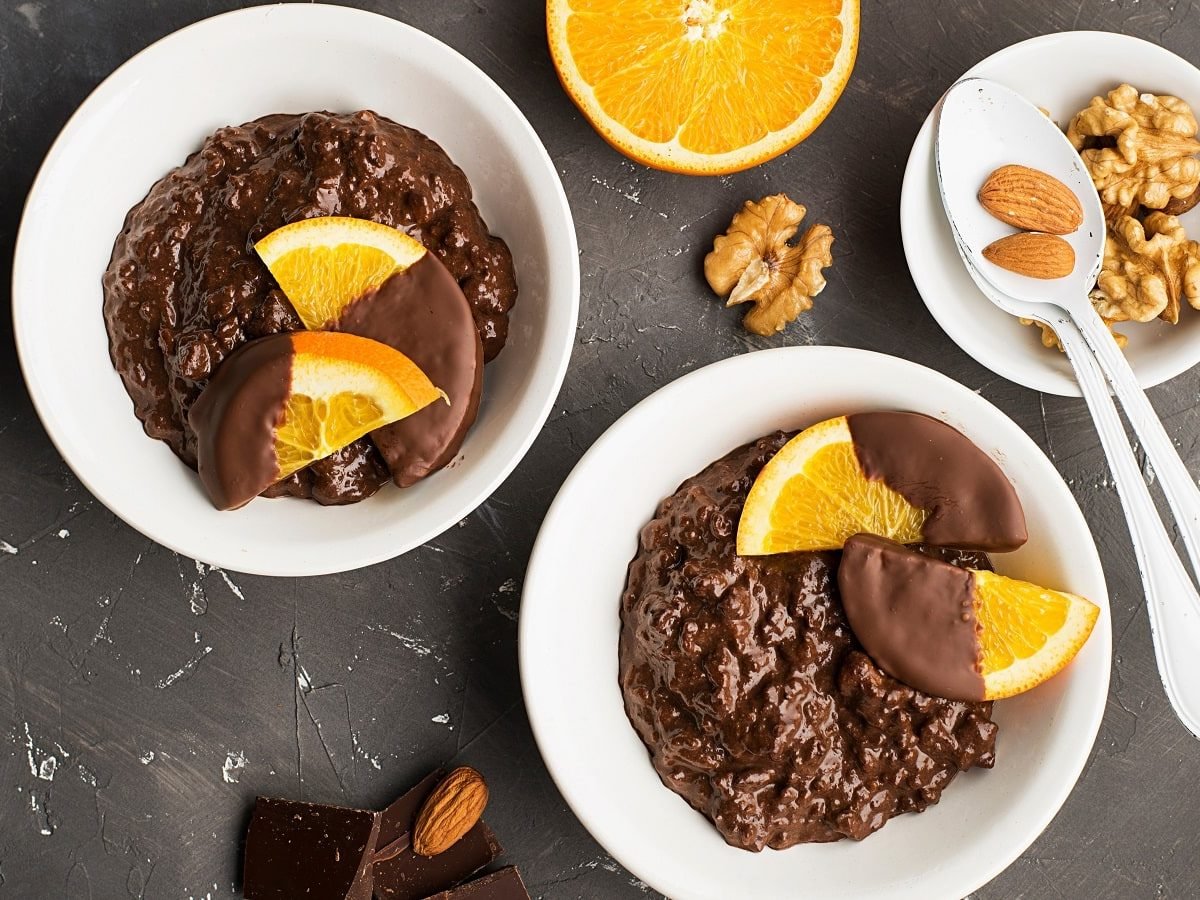 Zwei Schüsseln mit Orangen-Schoko-Porridge auf einem grauen Tisch.