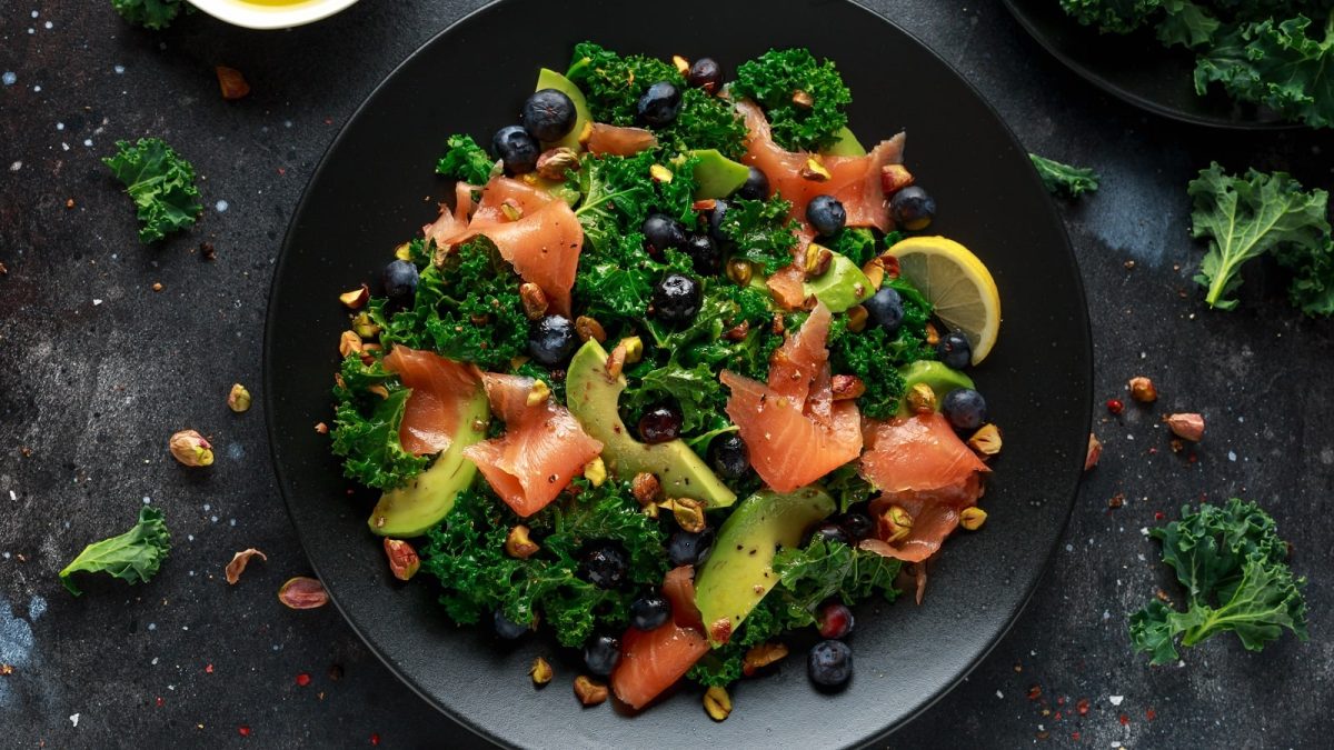 Ein schwarzer Teller mit Grünkohlsalat mit Lachs und Avocado.