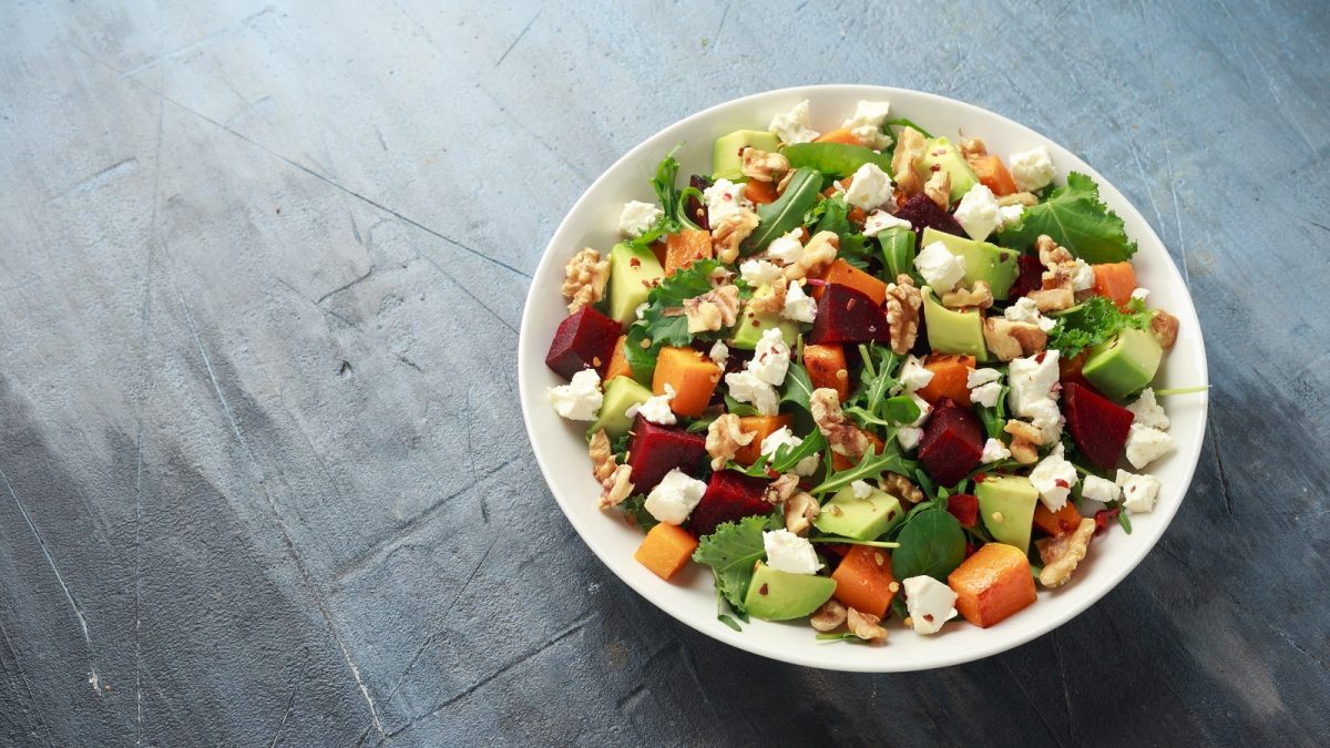 Ein weißer Teller mit einer Portion Kürbis-Bowl mit Rote Bete auf einem grauen Tisch.